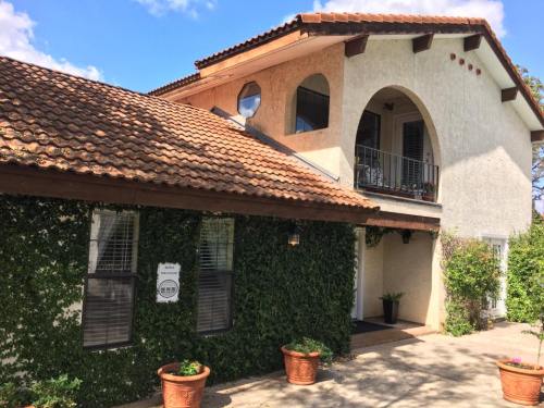 A two-story house with a tiled roof, ivy-covered walls, and a balcony, surrounded by potted plants.