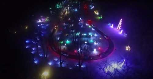 Aerial view of a colorful light display in a park, featuring illuminated trees and festive decorations at night.