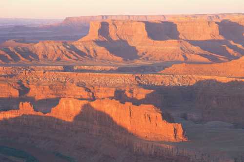 Sunset over rugged red rock formations, casting long shadows across the canyon landscape.