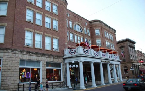 Historic brick building with large windows, decorative awnings, and flags, featuring a welcoming entrance.