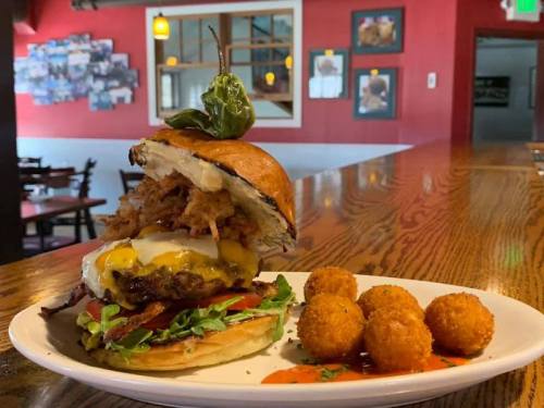 A towering burger with bacon, cheese, and crispy onion rings, served with golden tater tots on a plate.