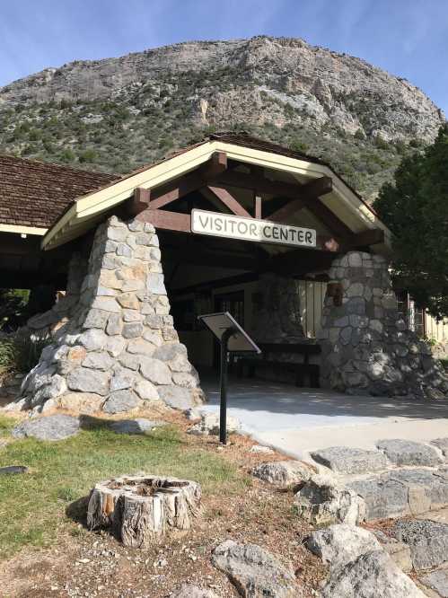 A stone visitor center with a sign, set against a backdrop of a large mountain under a clear sky.