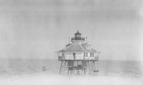 A vintage lighthouse standing on stilts over calm waters, shrouded in a soft, misty atmosphere.