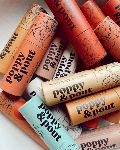 A collection of colorful lip balm tubes from Poppy & Pout, featuring various designs and shades stacked together.