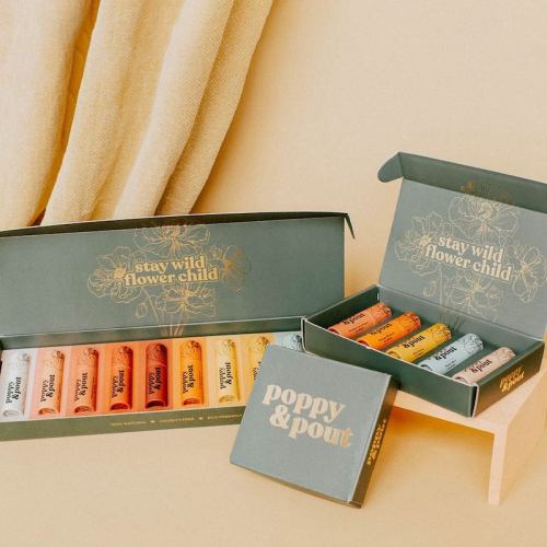 A collection of colorful lip balms in stylish packaging, displayed on a light background with soft fabric.