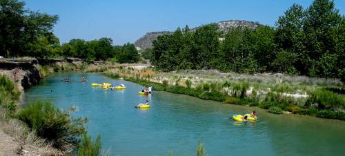 People floating on yellow rafts in a calm river surrounded by greenery and hills under a clear blue sky.