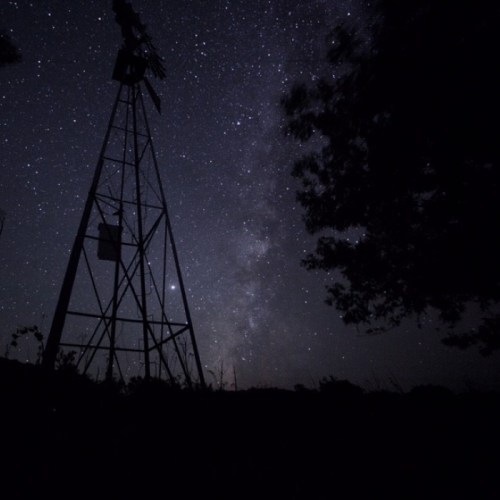 A silhouette of a windmill against a starry night sky, featuring the Milky Way and scattered stars.