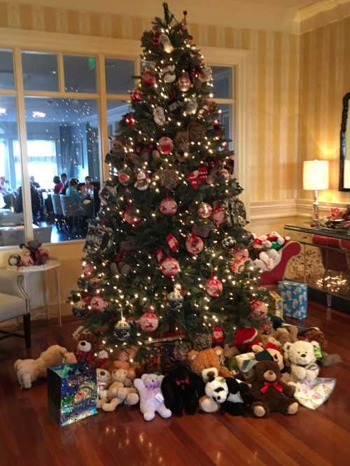 A decorated Christmas tree surrounded by stuffed animals and colorful gift boxes in a festive setting.