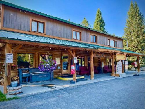 A rustic wooden building with a green roof, featuring flower baskets and outdoor seating, surrounded by trees.