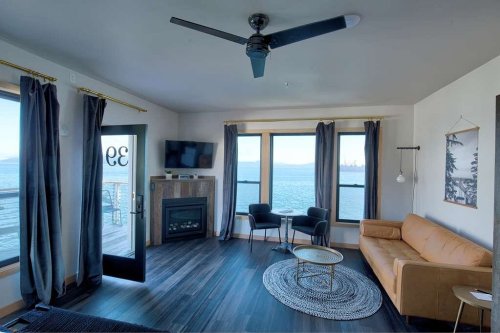 Cozy living room with a view of the water, featuring a sofa, TV, fireplace, and large windows with curtains.