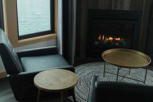 Cozy living space with two black chairs, a round table, and a fireplace, overlooking a serene water view.