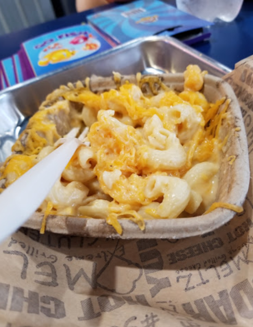 A serving of cheesy macaroni and cheese in a paper tray, with a plastic fork resting on top.
