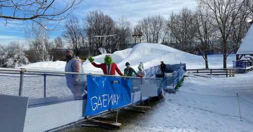 A snowy scene with people in costumes, including a character resembling the Grinch, near a winter attraction.