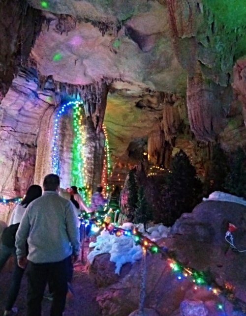 A group of people walking through a colorful, illuminated cave with festive lights and decorations.