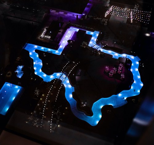 Aerial view of a pool shaped like Texas, illuminated with blue and purple lights at night.