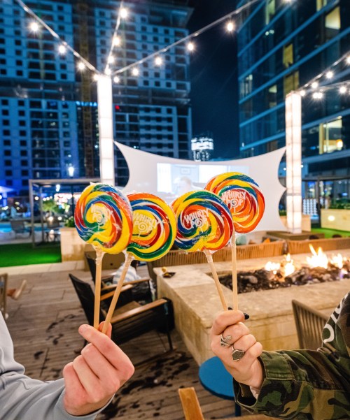 Colorful lollipops held up against a night backdrop with string lights and a fire pit in the foreground.