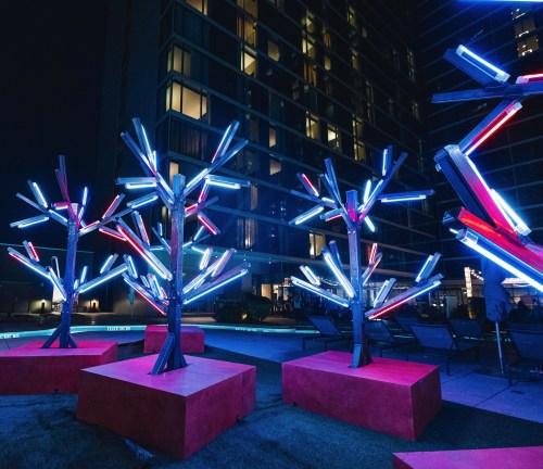 Colorful illuminated trees with neon lights in a modern outdoor space at night, beside a building.