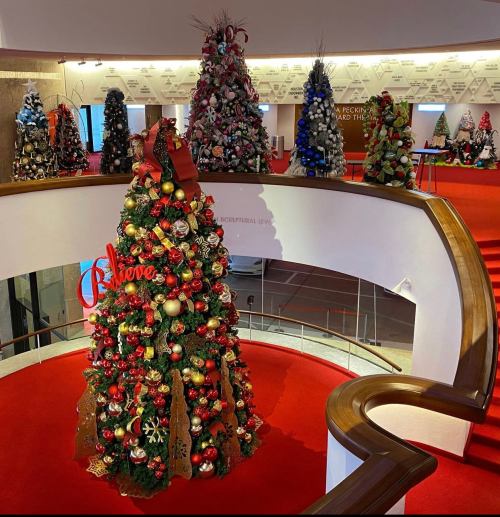A festive display of decorated Christmas trees in a circular atrium, with red carpet and holiday decorations.