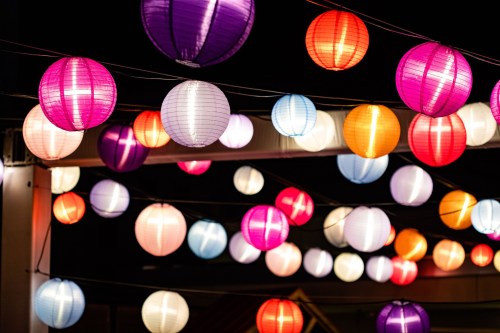 Colorful paper lanterns in various shades hang against a dark night sky, creating a festive atmosphere.