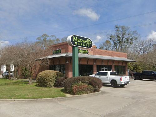 A brick building with a sign reading "Maxwell's Market," surrounded by greenery and parked cars.