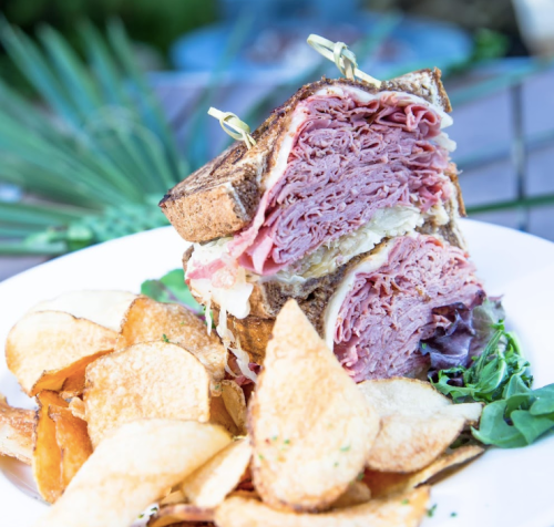 A stacked sandwich filled with layers of meat and sauerkraut, served with crispy potato chips on the side.