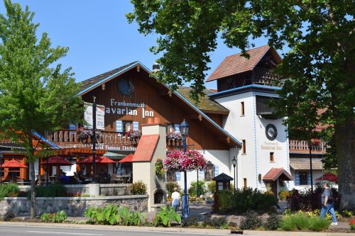 A charming Bavarian-style inn with colorful flowers, outdoor seating, and trees lining the street.