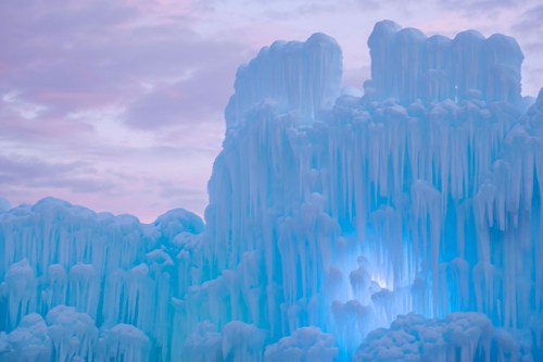 A stunning ice formation with blue lighting, featuring tall, jagged icicles against a pastel sky.