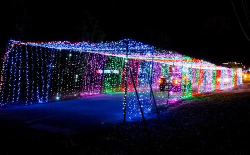 A colorful display of holiday lights drapes over a pathway, creating a festive atmosphere at night.