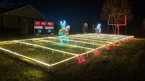 A festive outdoor display with colorful lights depicting a football field and players, celebrating a game night.