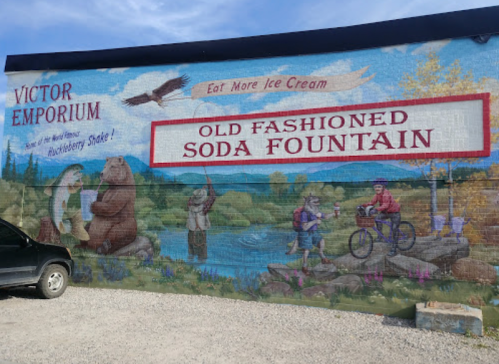 Mural on a building featuring animals, a bike, and text promoting ice cream and an old-fashioned soda fountain.