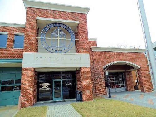 Exterior view of a brick fire station with a large emblem, featuring a driveway and grassy area in front.
