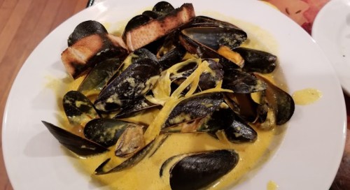 A plate of mussels in a creamy yellow sauce, garnished with lemon and served with toasted bread.