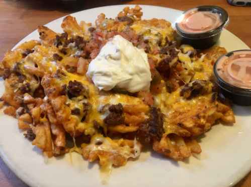 A plate of loaded nachos topped with cheese, ground beef, diced tomatoes, sour cream, and two dipping sauces.