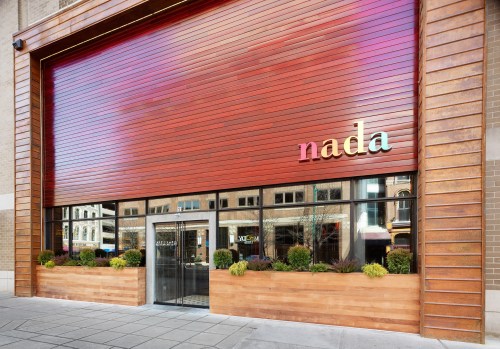 Exterior of a restaurant named "nada," featuring a large roll-up door and planters with greenery.