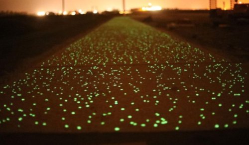 A glowing green pathway illuminated by small lights, set against a dark, nighttime background.