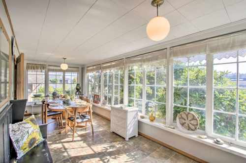 Bright sunroom with large windows, a dining table, and decorative elements, surrounded by greenery.