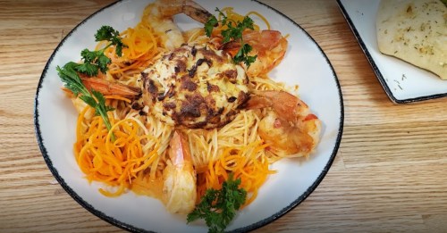 A plate of pasta topped with shrimp and a baked cheese crust, garnished with parsley and served with flatbread.