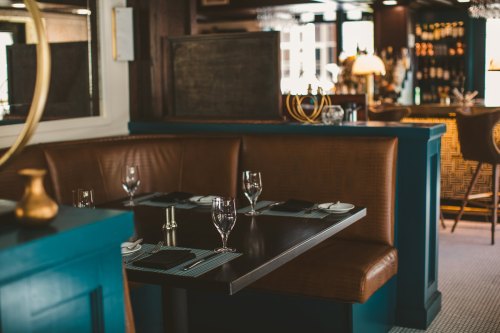 A cozy restaurant booth with a dark wooden table, elegant glassware, and a stylish bar in the background.