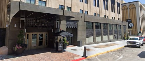 Exterior view of the Mesa Club building, featuring a modern entrance and sidewalk with parked cars.