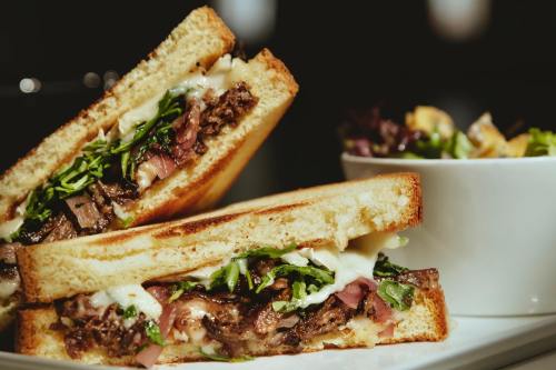 A close-up of a grilled sandwich filled with meat and greens, served with a side salad in a bowl.