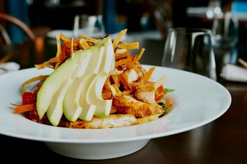 A plate of salad topped with sliced apples, crispy chicken, and colorful vegetables, served in a restaurant setting.