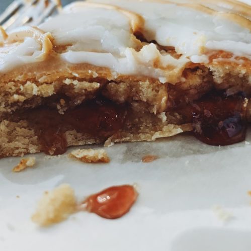 Close-up of a pastry with a golden crust, revealing a gooey filling and a drizzle of icing on top.