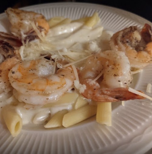 A plate of pasta with shrimp in a creamy sauce, garnished with grated cheese.