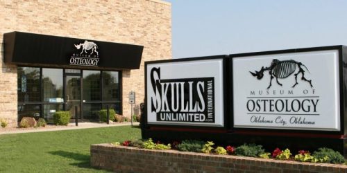 Exterior view of the Museum of Osteology in Oklahoma City, featuring a sign with a skeletal display and landscaping.