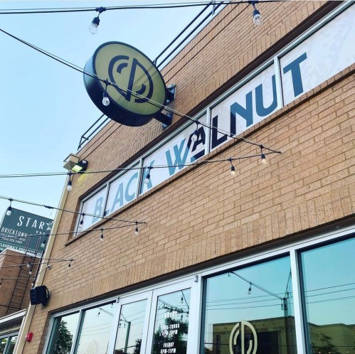 Exterior of a building featuring a sign that reads "Black Walnut," with string lights overhead.