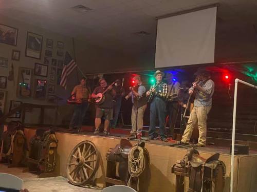 A group of musicians performs on stage with various instruments, surrounded by decorations and an American flag.