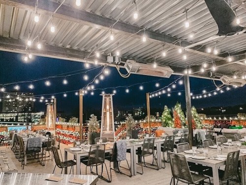 A rooftop dining area at night, adorned with string lights and festive decorations, featuring tables set for guests.