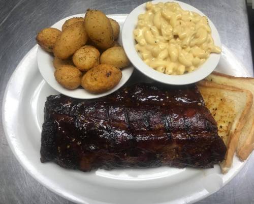 A plate featuring BBQ ribs, seasoned potatoes, macaroni and cheese, and toasted bread.