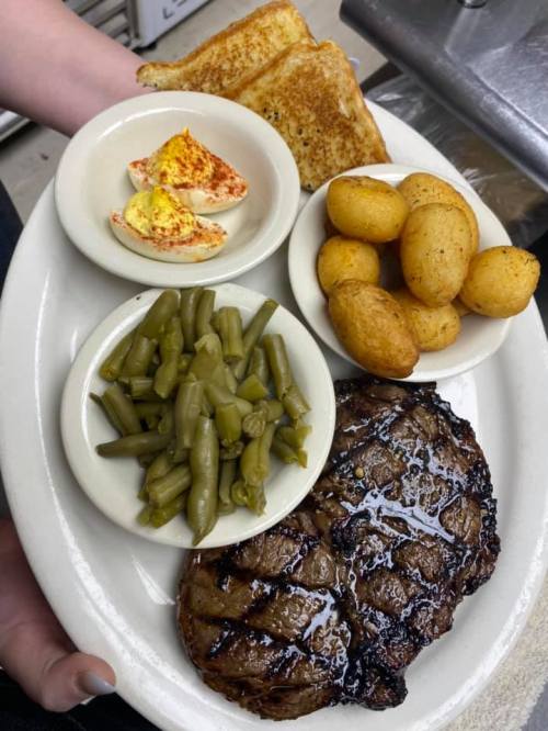 A plate with grilled steak, green beans, roasted potatoes, deviled eggs, and toasted bread.