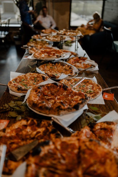 A long table filled with various pizzas, showcasing different toppings in a cozy restaurant setting.